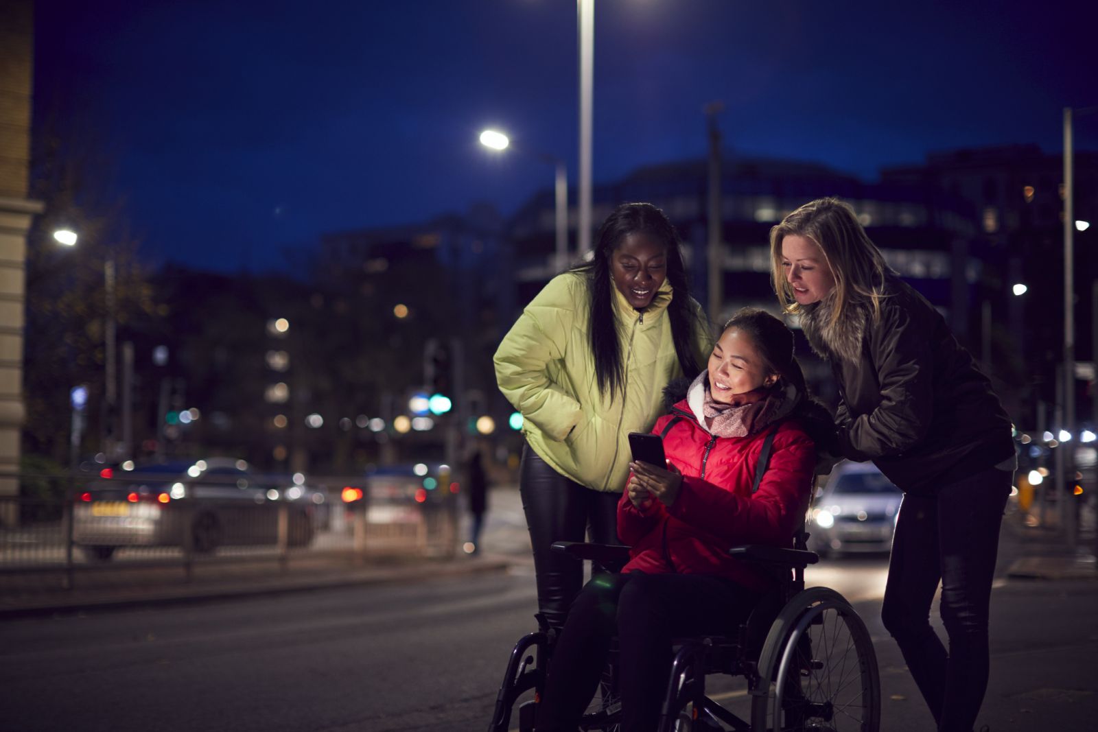 A young woman in a wheelchair talking to two friends at night in the city banner image