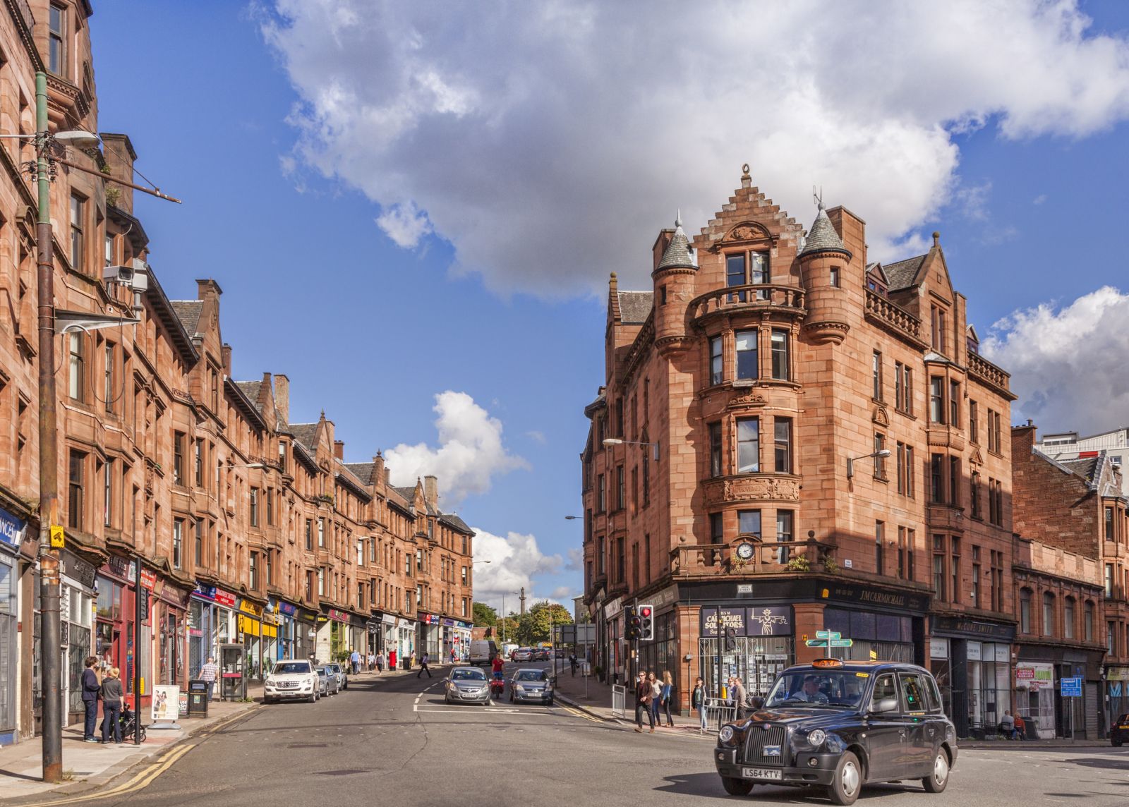 High St Glasgow, busy road with red sandstone tenement flats either side and shops on the ground floor banner image