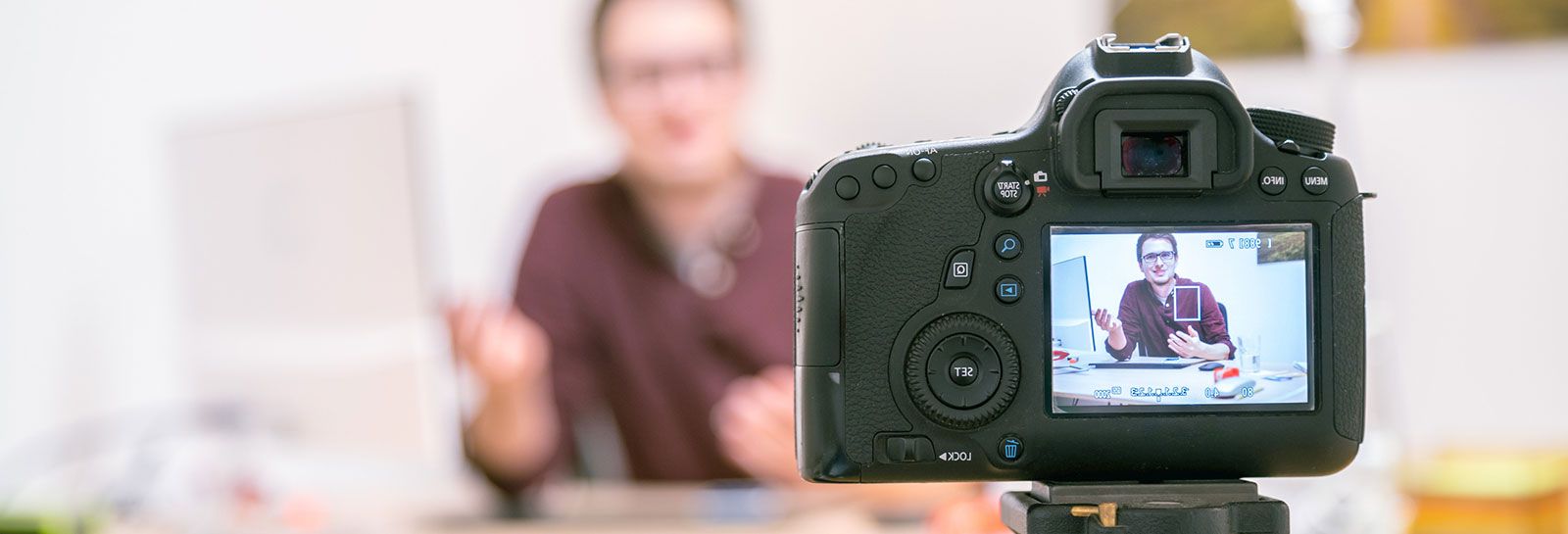 Camera on tripod is filming a young man sitting at a desk banner image