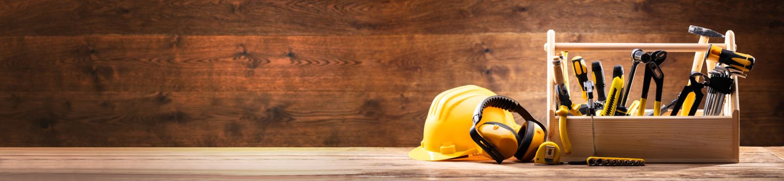 Yellow hard hat and tool box full of tools on a wooden bench banner image