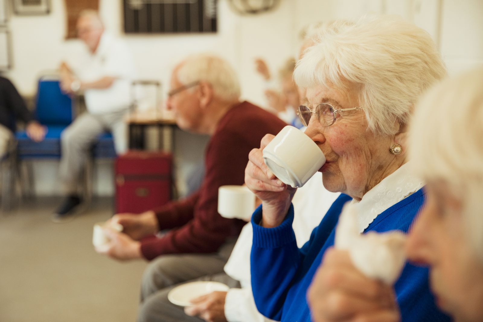 Older woman drinking cup of tea at social event banner image